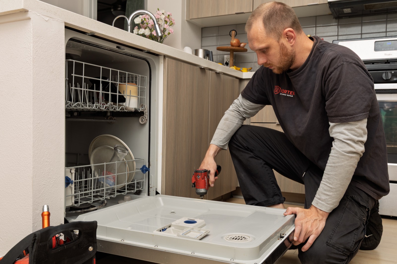 Technician repairing a dishwasher door with a power drill